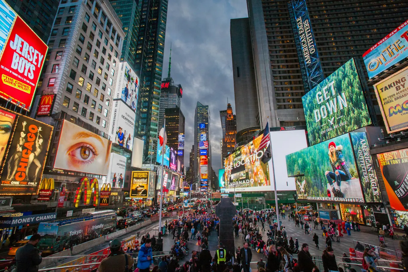 times square NY with a lot of neon lighted ads and people walking around - 1366x911